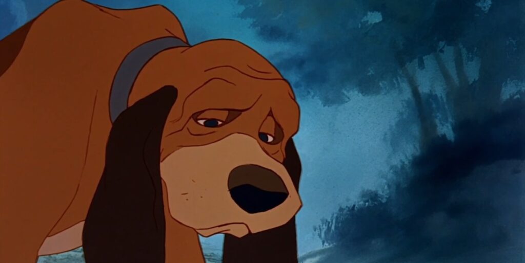 Dorosły pies Miedziak uwiązany przy budzie rozmawia z lisem Todem.